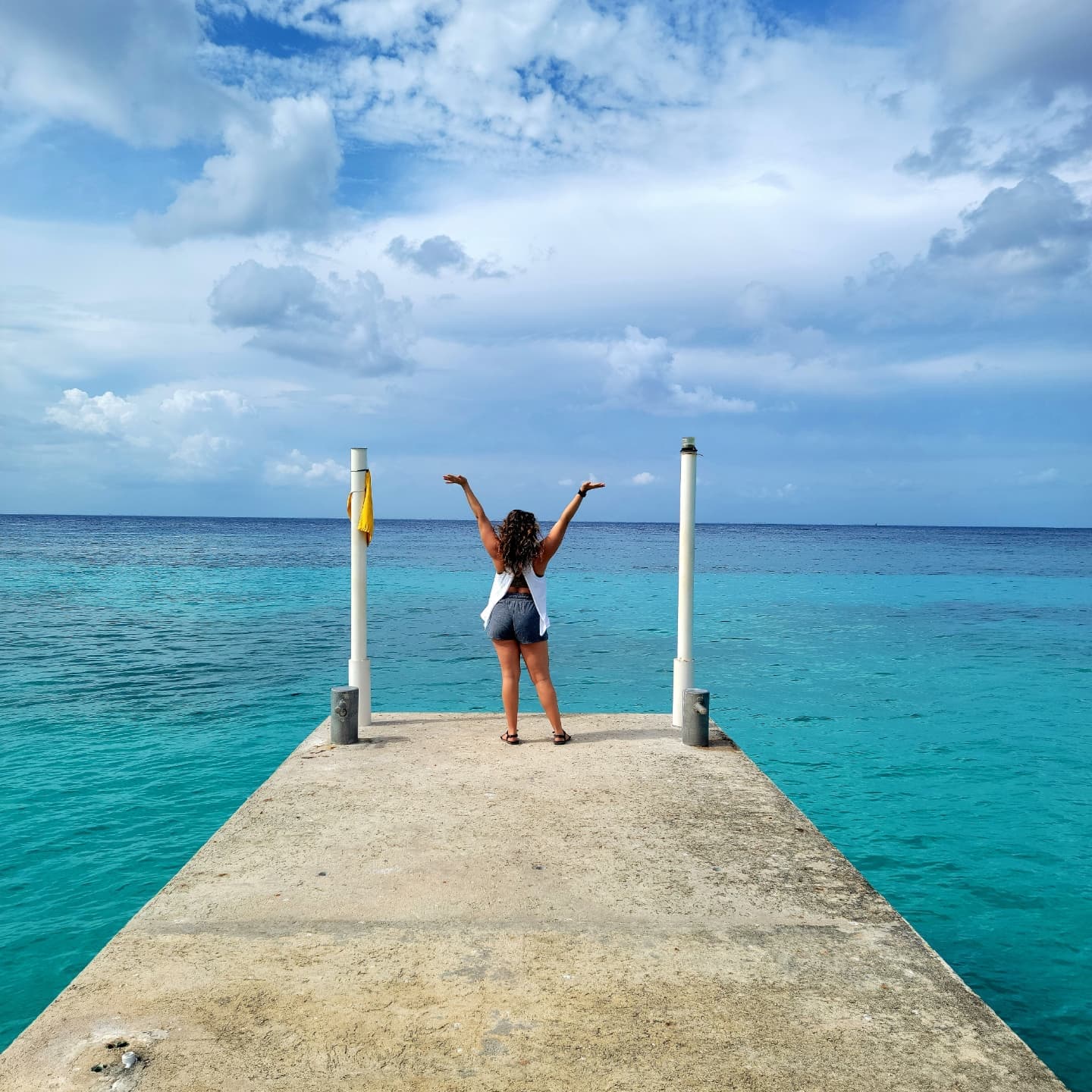 Jessie with arms raised at the end of an ocean pier